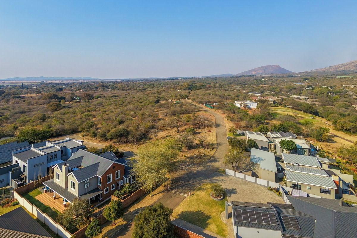 An aerial view of a residential estate featuring paved roads, modern homes with solar panels, and surrounding natural landscape.