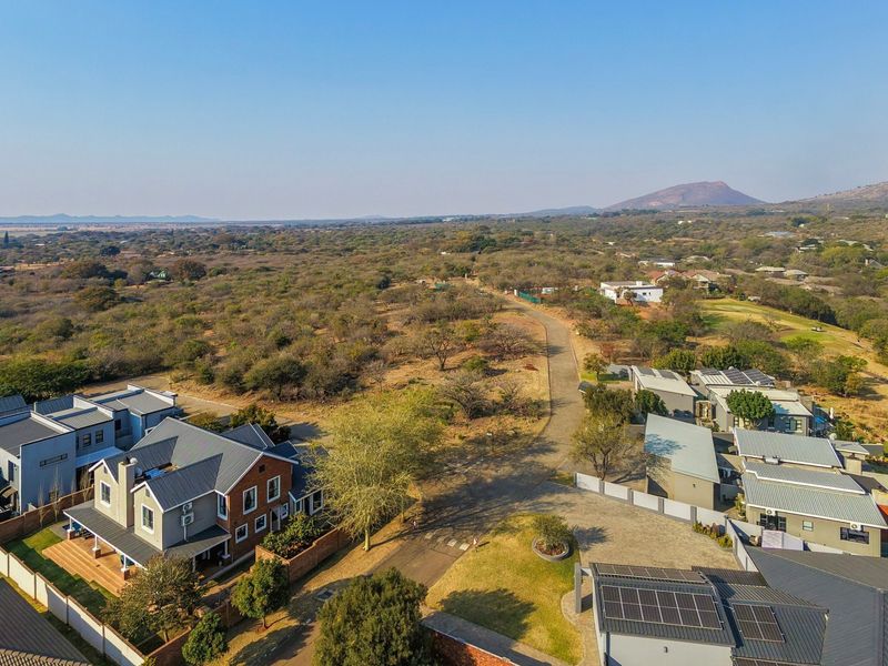 An aerial view of a residential estate featuring paved roads, modern homes with solar panels, and surrounding natural landscape.