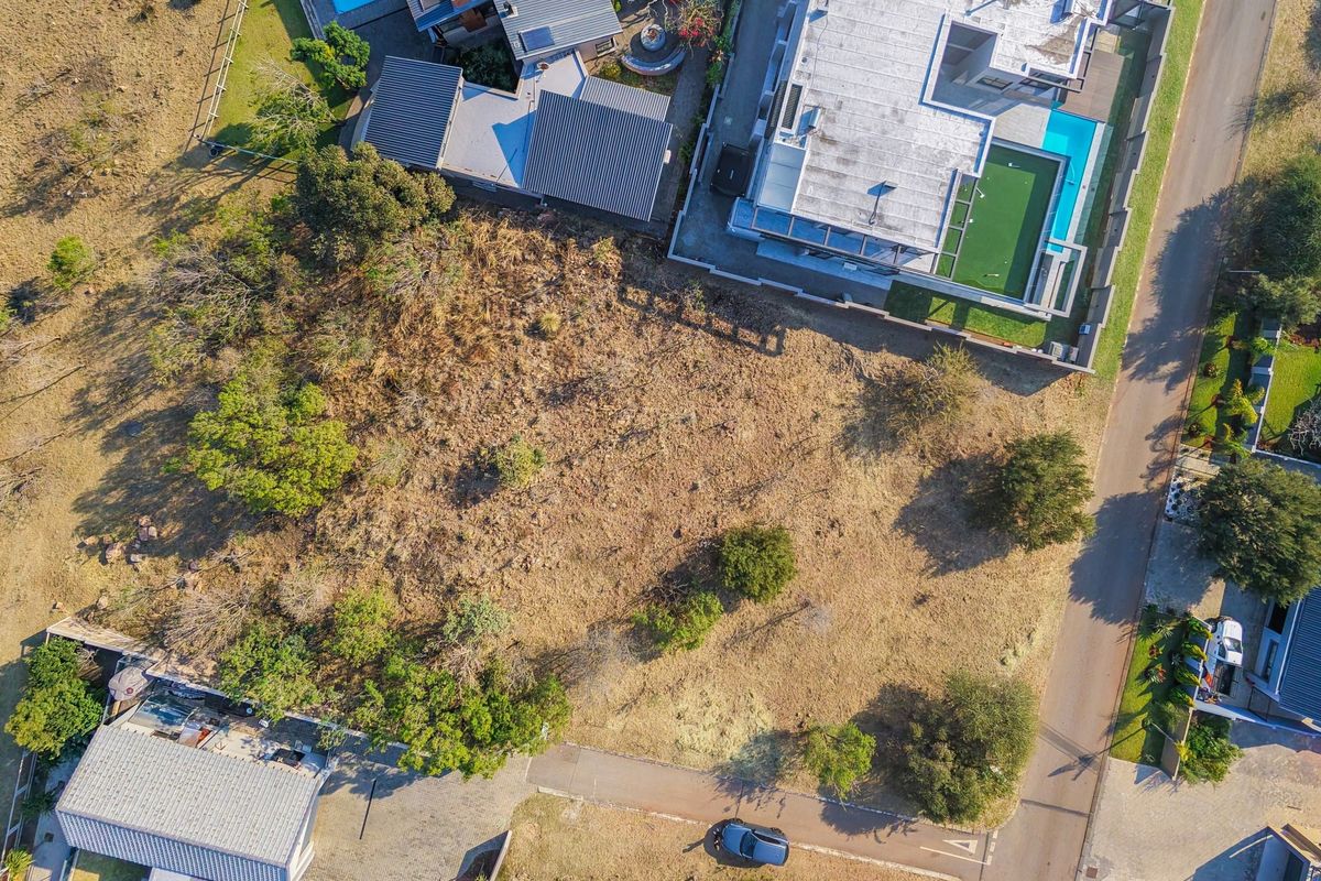 An aerial view of a vacant residential plot situated within an established neighborhood, featuring natural vegetation and proximity to existing residential infrastructure.