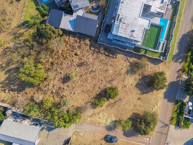 An aerial view of a vacant residential plot situated within an established neighborhood, featuring natural vegetation and proximity to existing residential infrastructure.