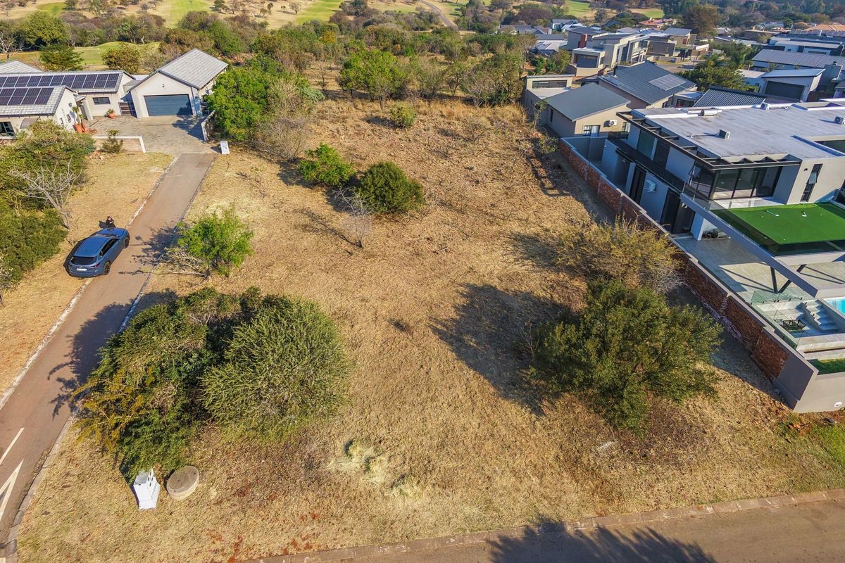 An aerial view of a vacant residential plot situated within an established estate, featuring mature trees and direct access to a paved road.