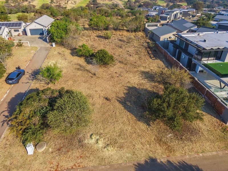 An aerial view of a vacant residential plot situated within an established estate, featuring mature trees and direct access to a paved road.