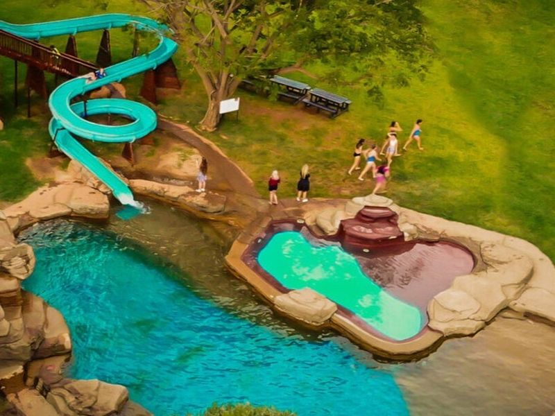 Aerial view of a recreational pool area featuring a large water slide, rock-scaped pool edges, and landscaped grounds.