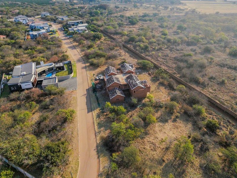 Aerial view of a residential plot featuring an unfinished brick building structure within a developing estate.