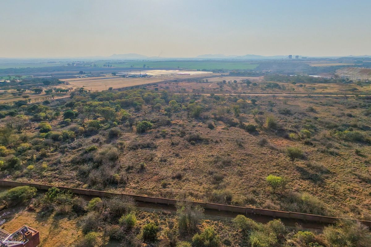 An aerial view of a large, undeveloped residential land plot featuring natural vegetation and a perimeter boundary wall.