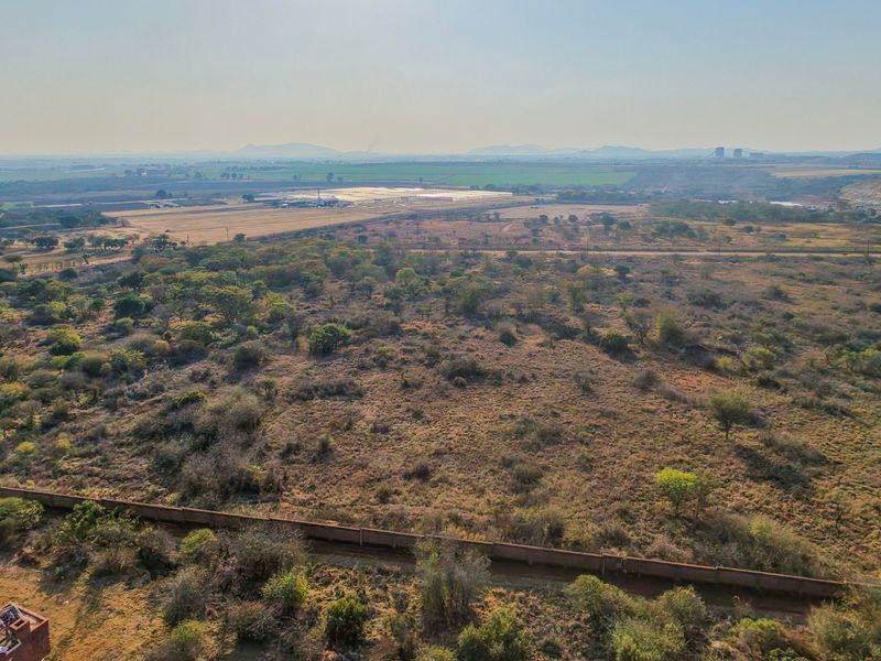 An aerial view of a large, undeveloped residential land plot featuring natural vegetation and a perimeter boundary wall.