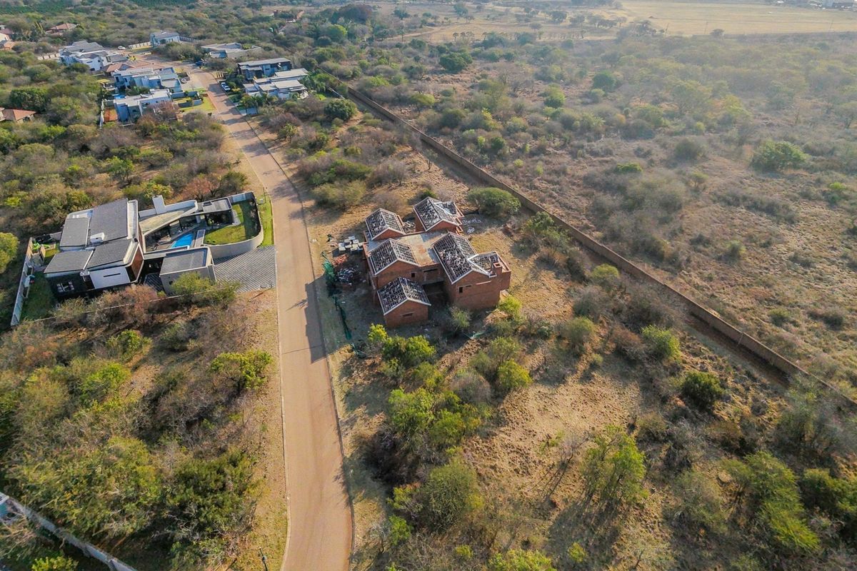 Aerial view of a residential plot featuring an unfinished brick building structure with exposed roof trusses, situated in a developing estate.