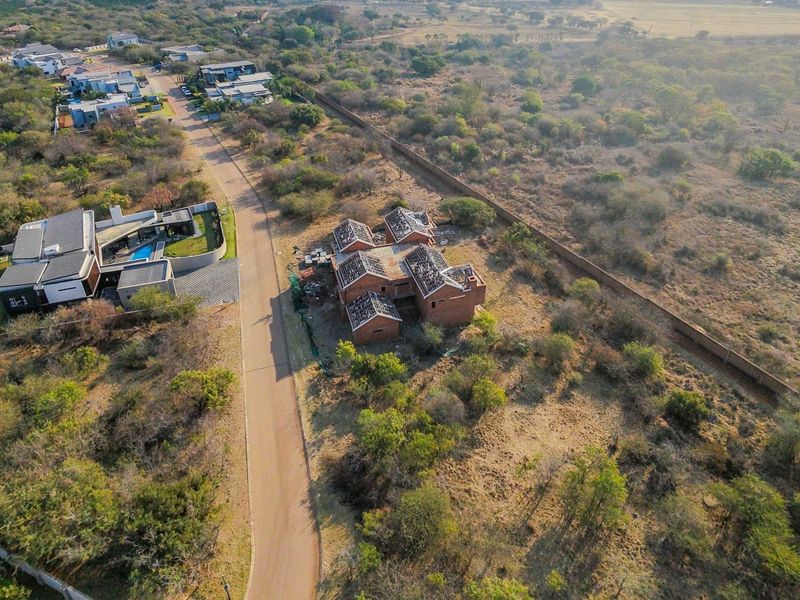 Aerial view of a residential plot featuring an unfinished brick building structure with exposed roof trusses, situated in a developing estate.