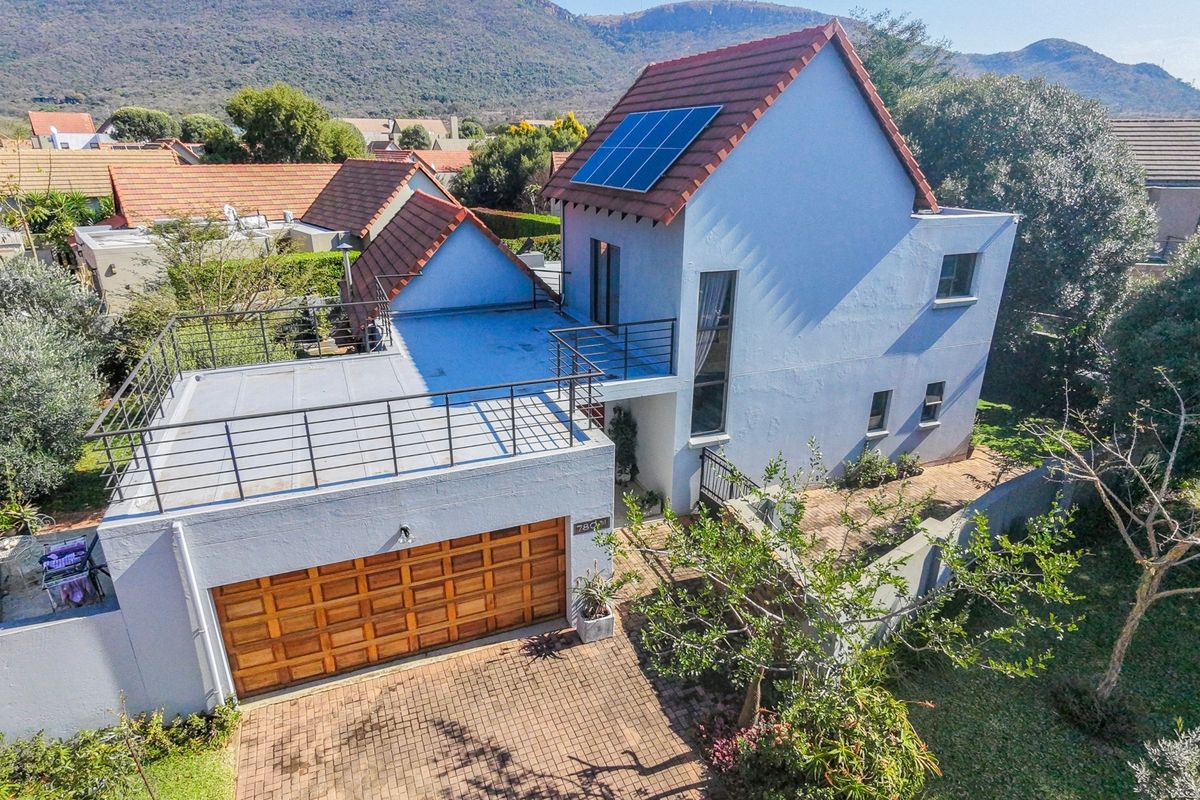 Aerial view of a two-story residential property featuring a tiled roof with solar panels, a balcony, and a paved driveway with a garage.