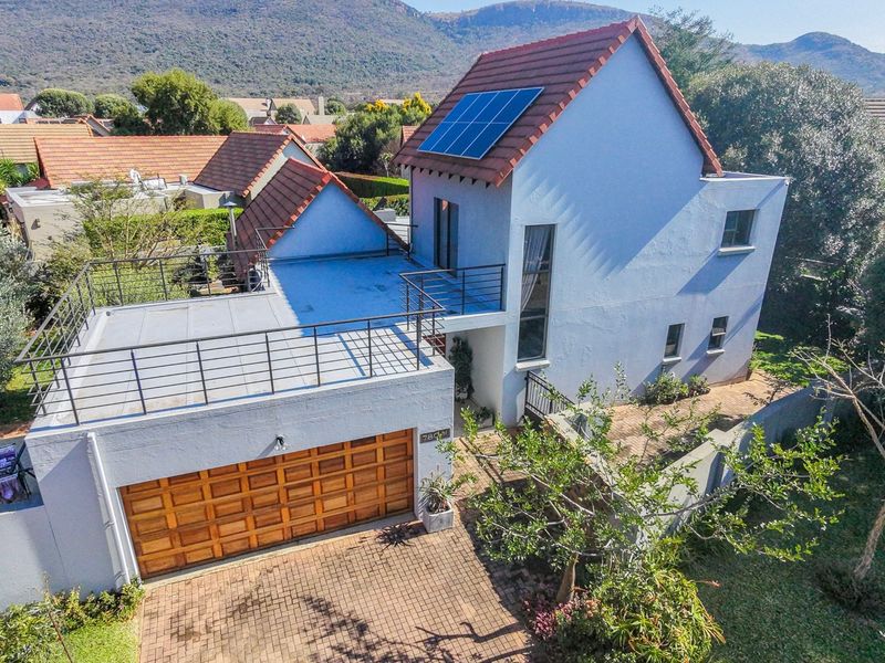 Aerial view of a two-story residential property featuring a tiled roof with solar panels, a balcony, and a paved driveway with a garage.