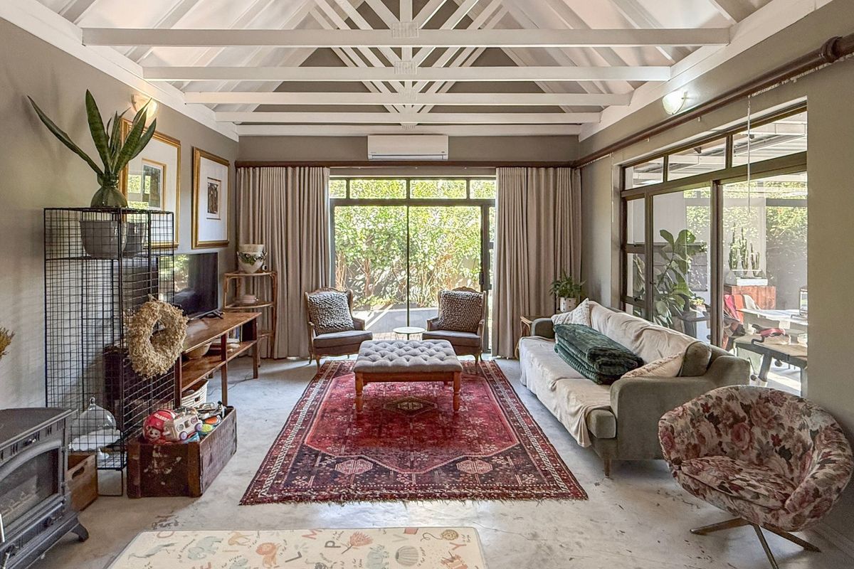 Spacious living room featuring a vaulted ceiling with exposed trusses, polished concrete floors, a wood-burning stove, and large sliding doors opening to the garden.