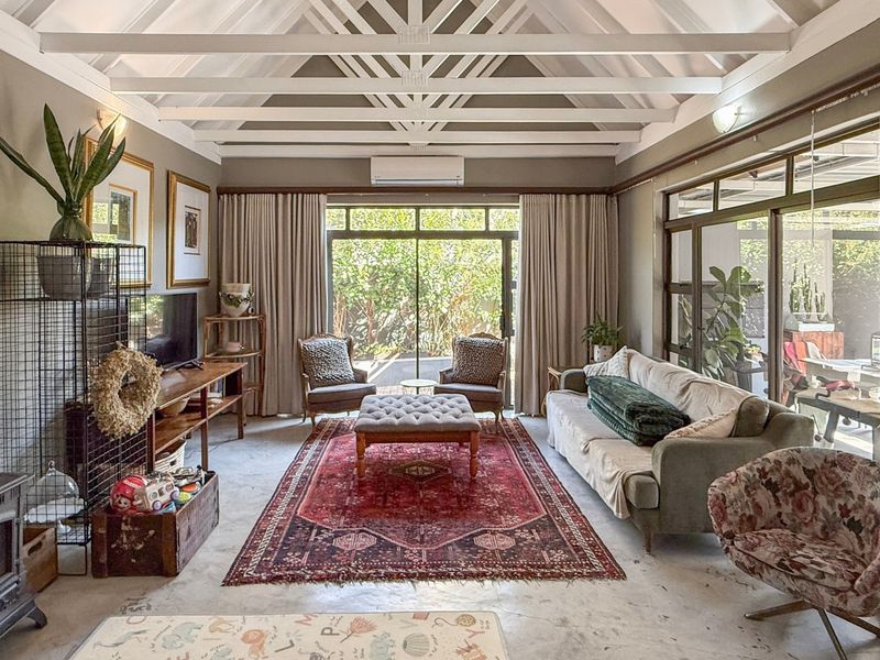 Spacious living room featuring a vaulted ceiling with exposed trusses, polished concrete floors, a wood-burning stove, and large sliding doors opening to the garden.