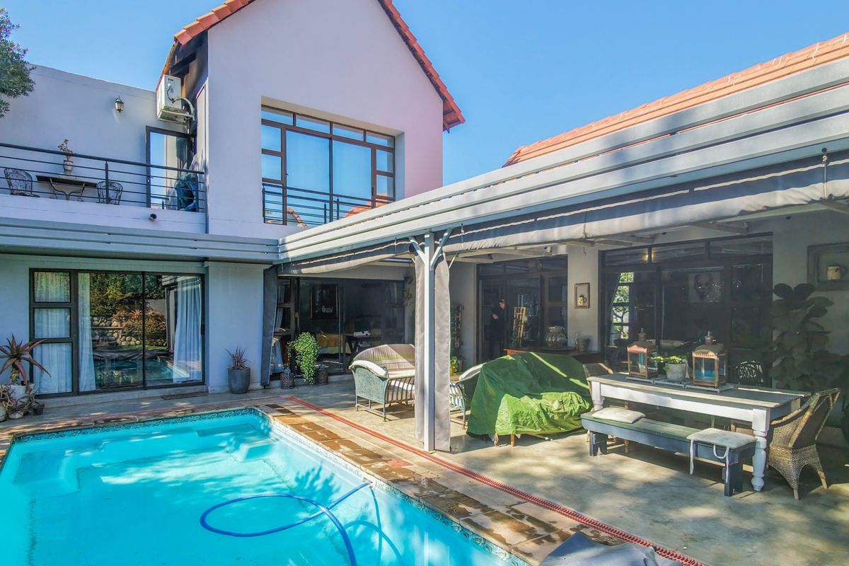 Rear exterior view featuring a swimming pool, a spacious covered patio area, and an upper-level balcony with sliding door access to the home.
