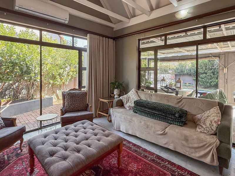 A bright living room featuring a vaulted ceiling with exposed rafters, large sliding glass doors providing garden access, and a wall-mounted air conditioning unit.