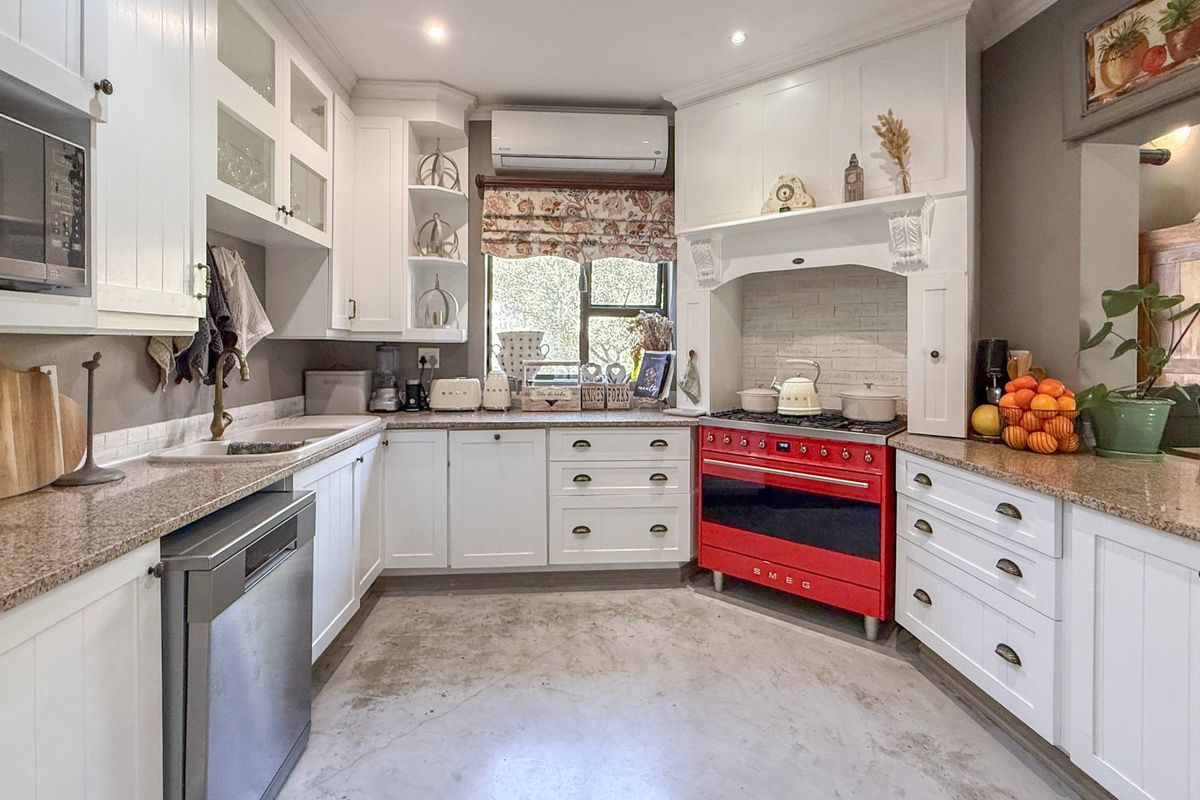 A well-appointed kitchen featuring white cabinetry, granite countertops, a striking red Smeg gas stove, and integrated appliances with a durable concrete floor.