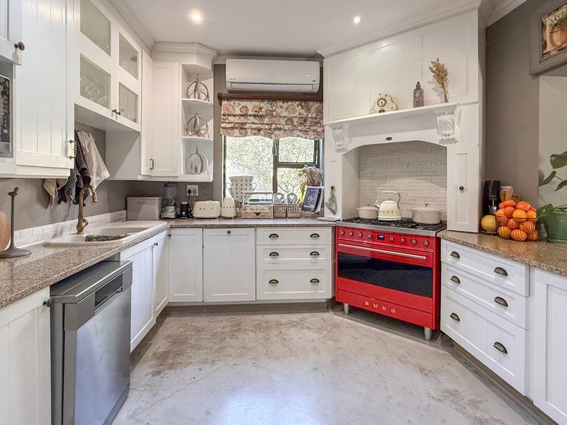 A well-appointed kitchen featuring white cabinetry, granite countertops, a striking red Smeg gas stove, and integrated appliances with a durable concrete floor.