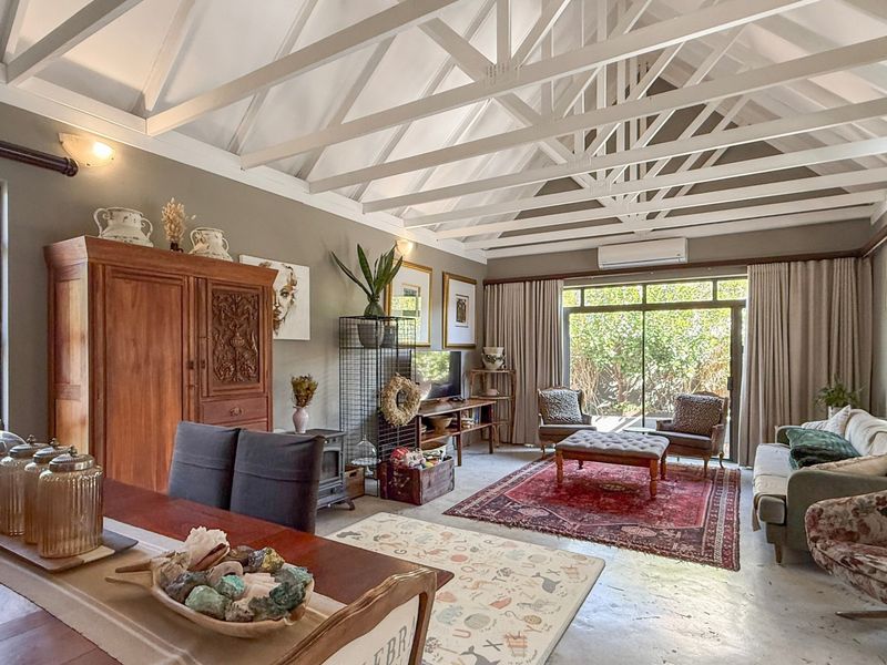 Spacious open-plan living and dining area featuring high vaulted ceilings with exposed white timber trusses and polished concrete floors.