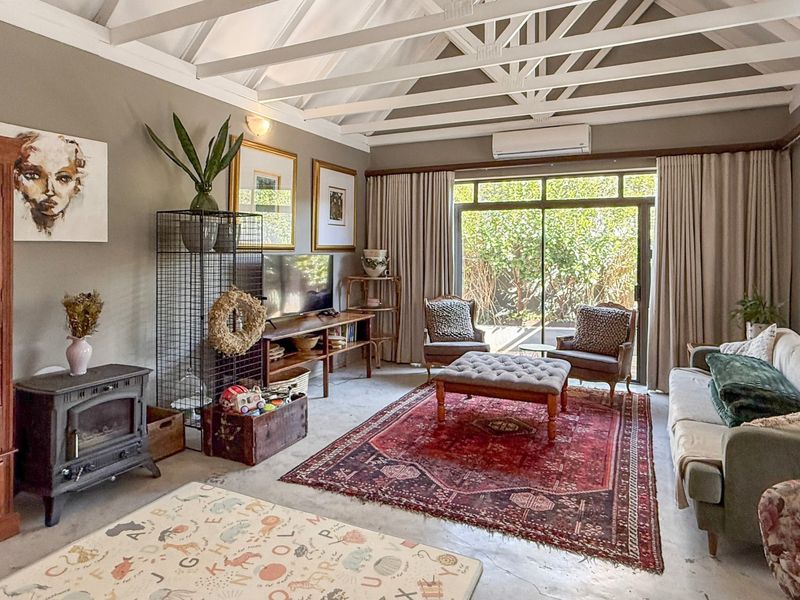 Spacious living room featuring a vaulted ceiling with exposed timber rafters, a cast iron fireplace, and large sliding glass doors opening to the garden.