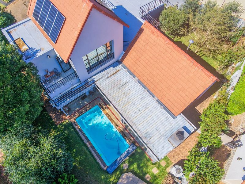 Aerial view of the property featuring a swimming pool, tiled roof with solar panels, and a spacious garden area.