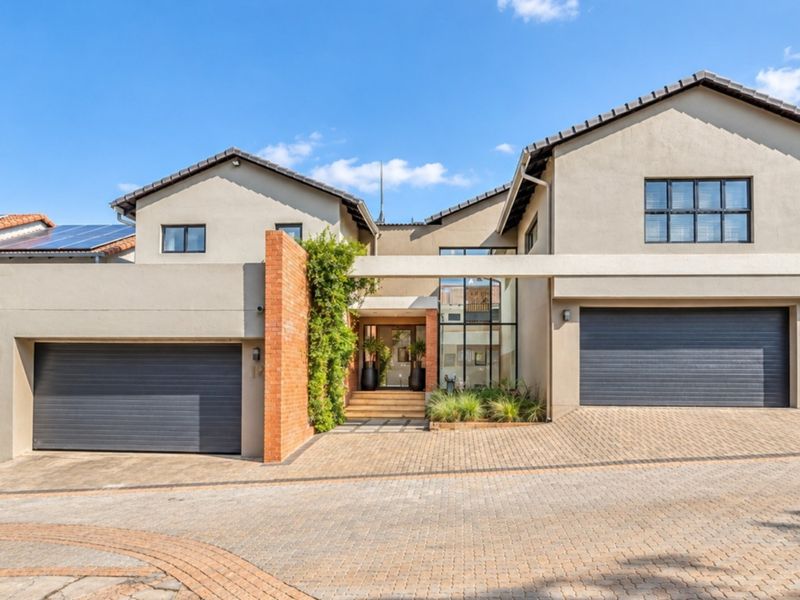 Modern double-story residence featuring a paved driveway, double garage, solar panels, and a striking brick feature wall at the entrance.