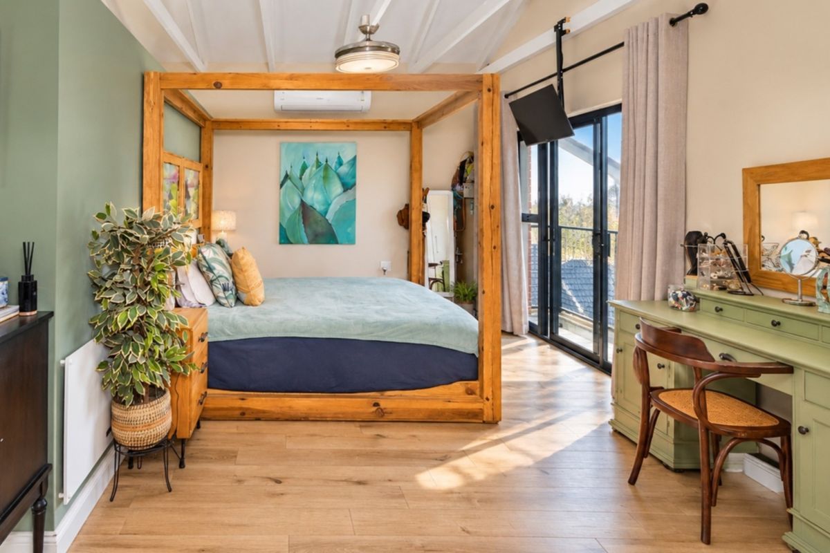 A well-maintained bedroom featuring exposed beam ceilings, laminate flooring, and large sliding glass doors that provide natural light and access to the outdoors.