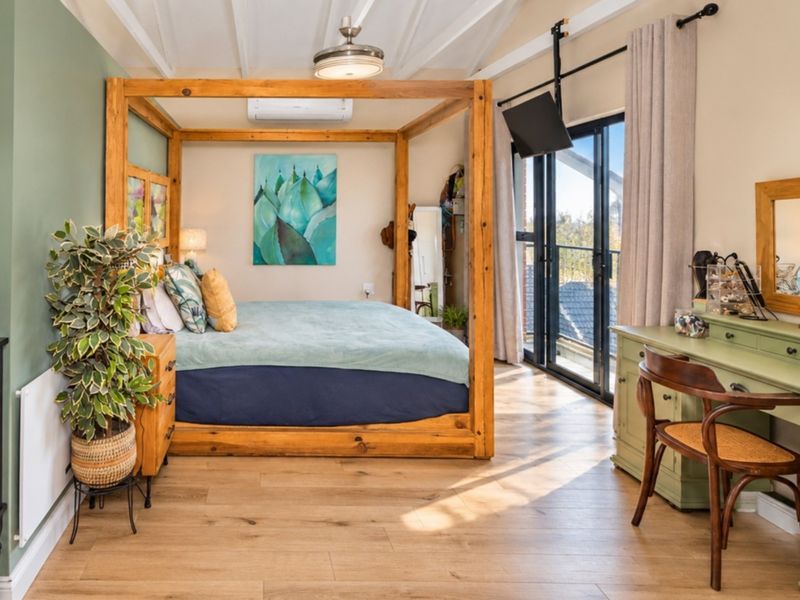 A well-maintained bedroom featuring exposed beam ceilings, laminate flooring, and large sliding glass doors that provide natural light and access to the outdoors.