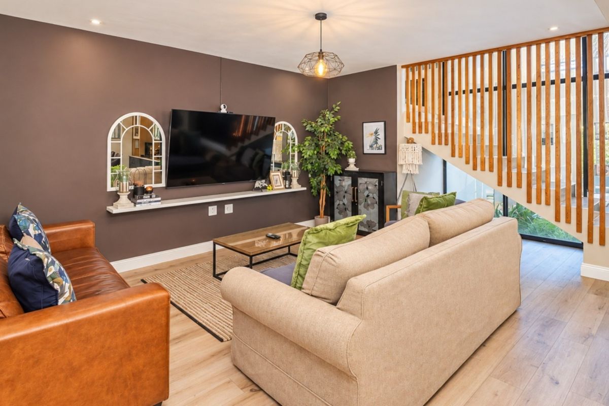 A well-maintained living room featuring timber staircase detailing, laminate flooring, and modern lighting fixtures, creating a warm and inviting atmosphere.