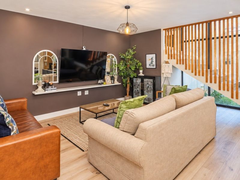 A well-maintained living room featuring timber staircase detailing, laminate flooring, and modern lighting fixtures, creating a warm and inviting atmosphere.