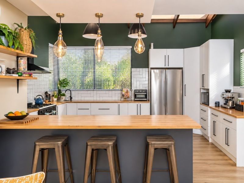 Modern kitchen featuring white cabinetry, wooden countertops, subway tile backsplash, integrated appliances, and a central island with pendant lighting under a skylight.
