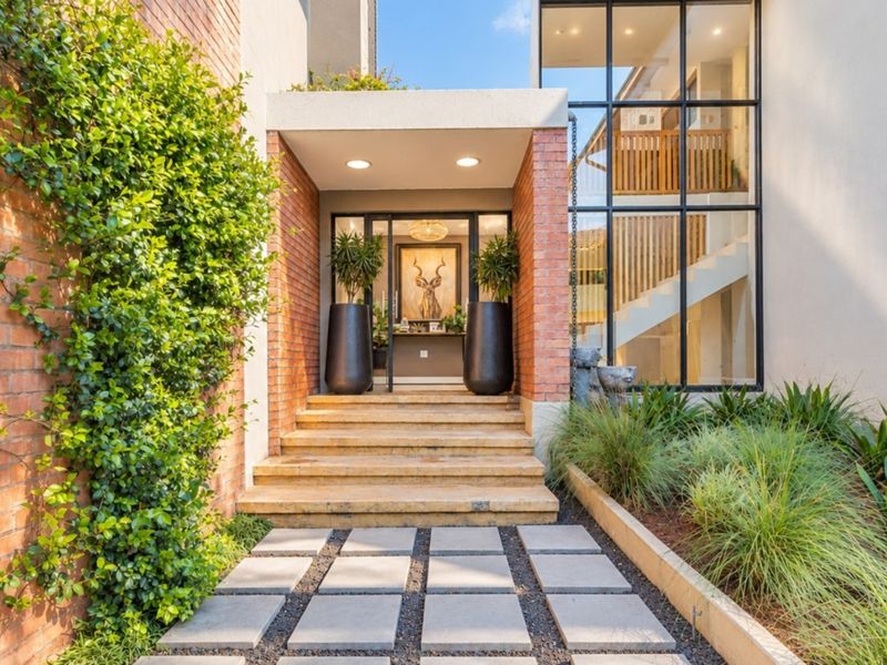 Modern front entrance featuring a brick facade, stone steps, and large glass windows, complemented by a landscaped garden and paver walkway.