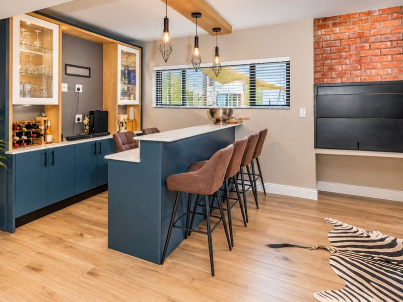 Modern entertainment bar area featuring custom blue cabinetry, stone countertops, integrated wine storage, and a built-in braai set against an exposed brick wall.