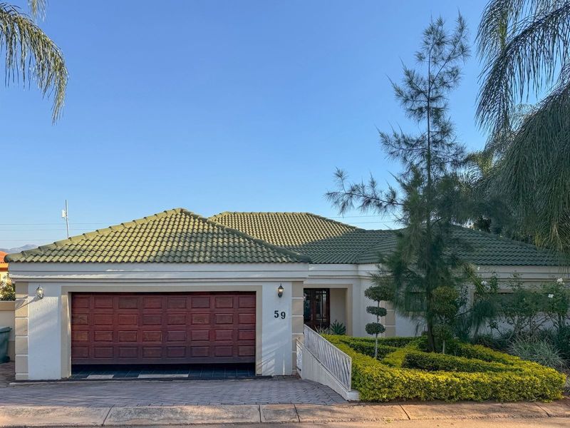 Front elevation of a well-maintained house featuring a tiled roof, double garage, paved driveway, and manicured garden landscaping.