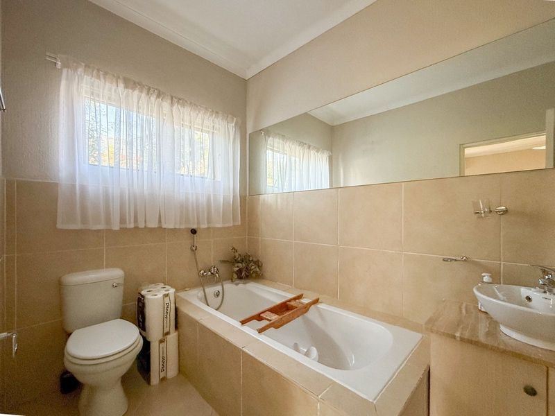A functional bathroom featuring a built-in bathtub, wall-mounted toilet, vanity basin, and large wall mirror with neutral tiled finishes.