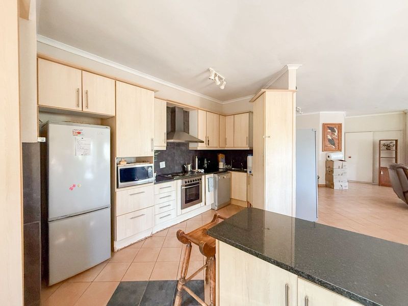 Functional kitchen featuring light wood cabinetry, granite countertops, built-in oven, and a central island, flowing into an open-plan living area.
