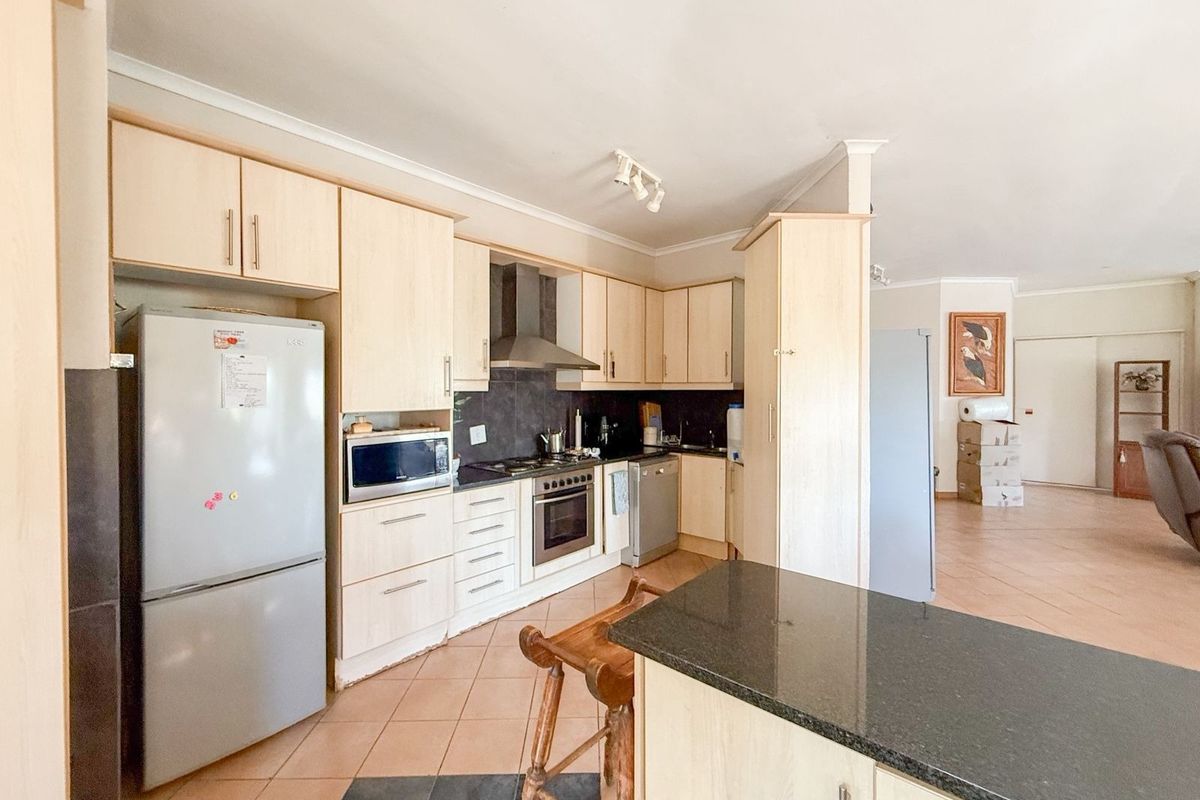 Functional kitchen featuring light wood cabinetry, granite countertops, built-in oven, and a central island, flowing into an open-plan living area.