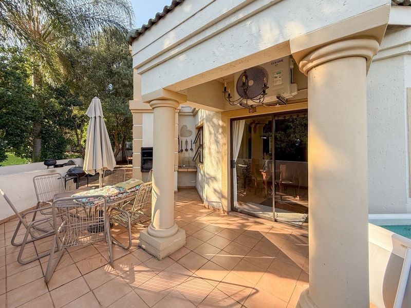 Covered patio area featuring tiled flooring, built-in braai, and decorative columns, providing direct access to the interior through sliding glass doors.