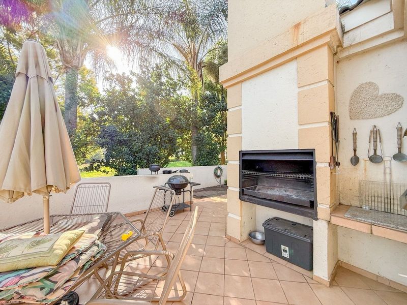 Covered patio area featuring a built-in braai, tiled flooring, and a low perimeter wall, overlooking a garden setting.