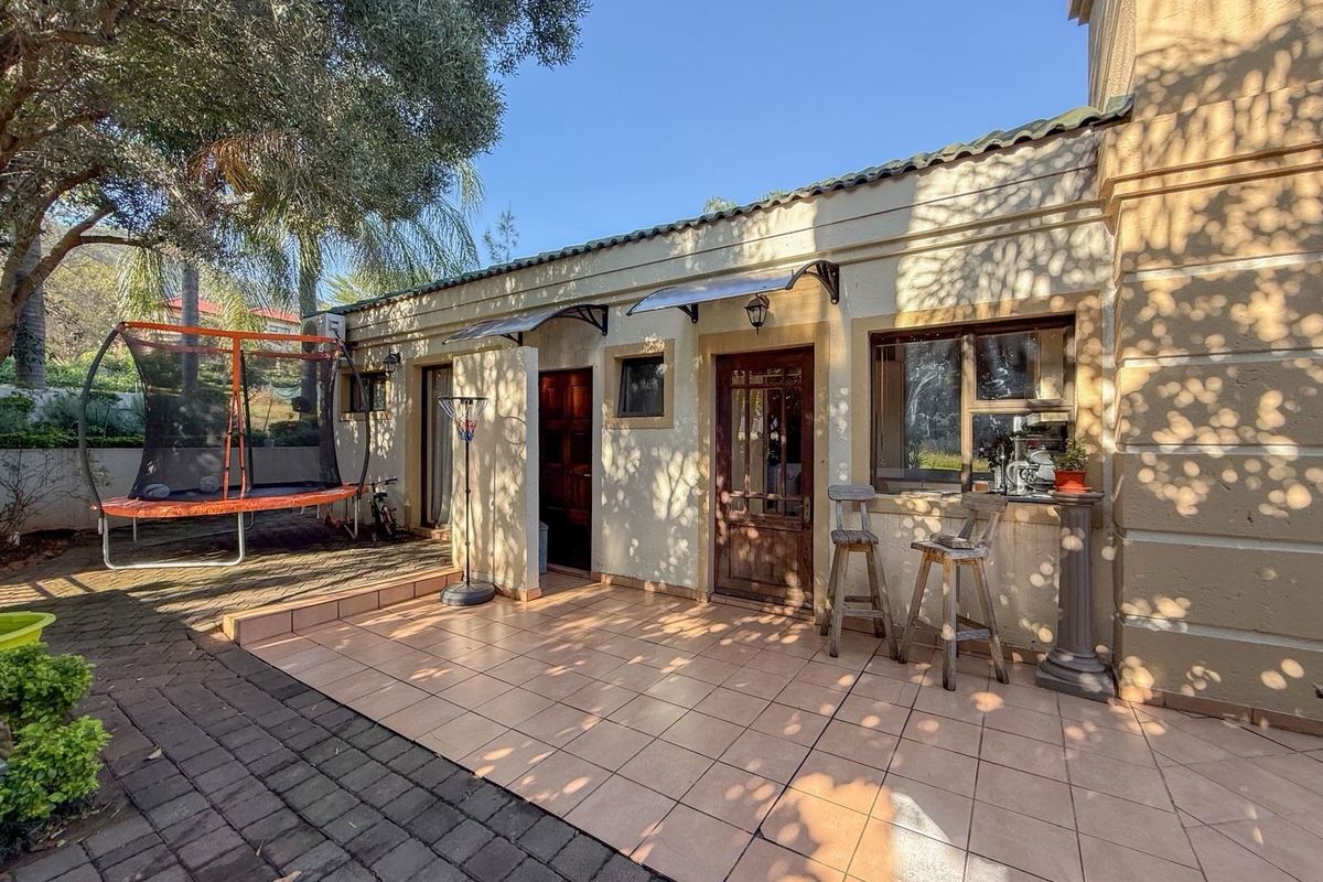 A rear exterior view featuring a tiled patio area, paved pathways, and access to the home through timber doors with protective window awnings.