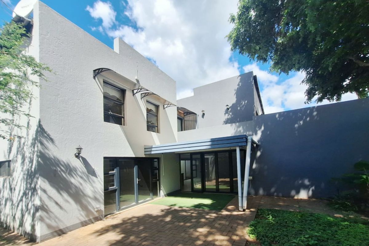 Rear view of the townhouse featuring a paved patio area, covered outdoor space, and modern aluminium sliding doors leading into the home.