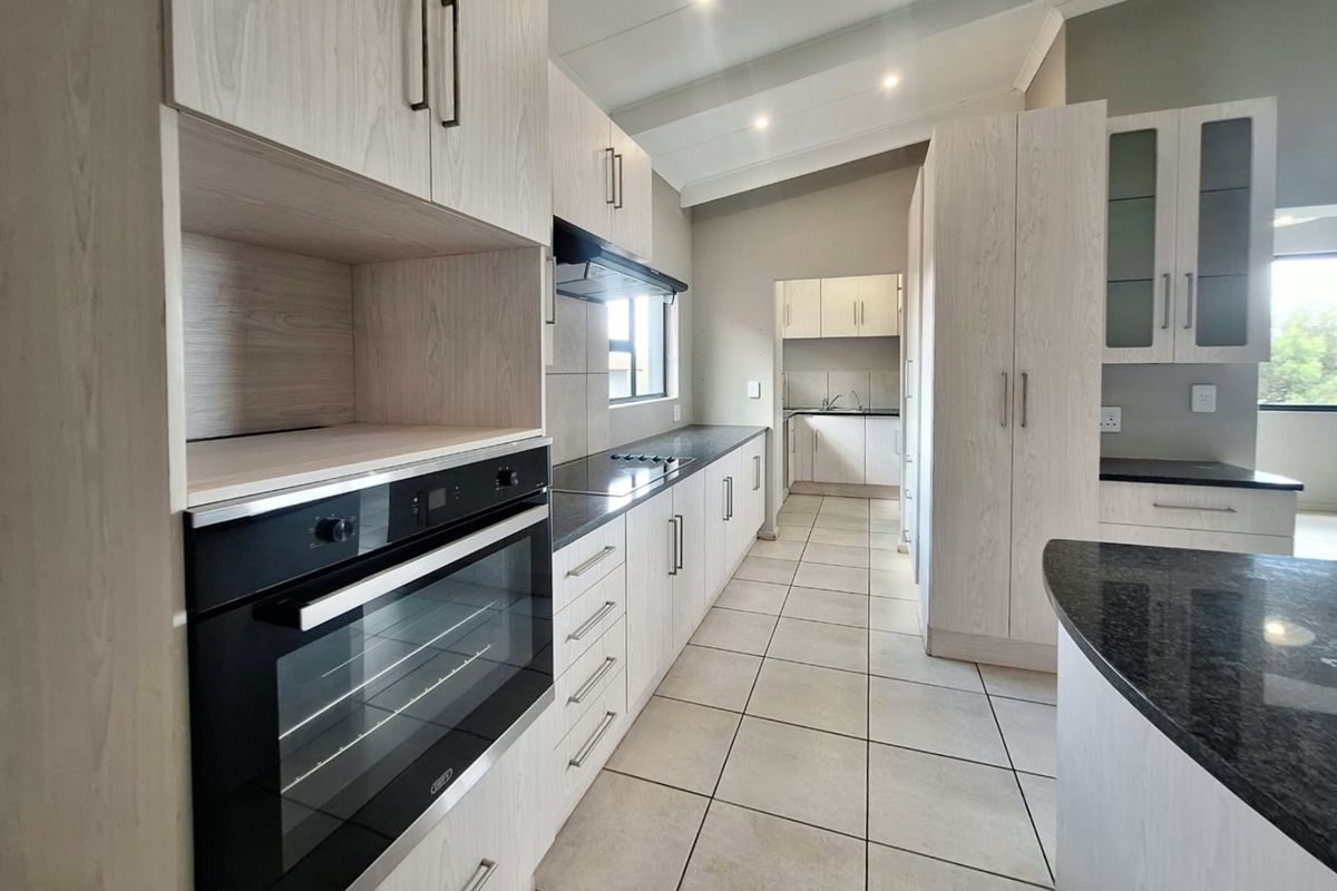Modern kitchen featuring light wood-grain cabinetry, dark granite countertops, built-in oven, hob, and extractor fan, with tiled flooring and a connected scullery area.