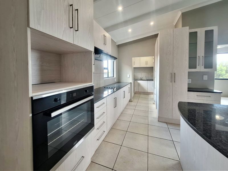 Modern kitchen featuring light wood-grain cabinetry, dark granite countertops, built-in oven, hob, and extractor fan, with tiled flooring and a connected scullery area.