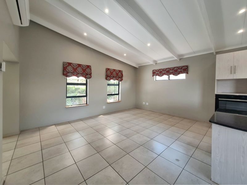 Spacious open-plan living area featuring tiled floors, exposed beam ceilings with recessed lighting, and a modern kitchen corner with built-in oven.