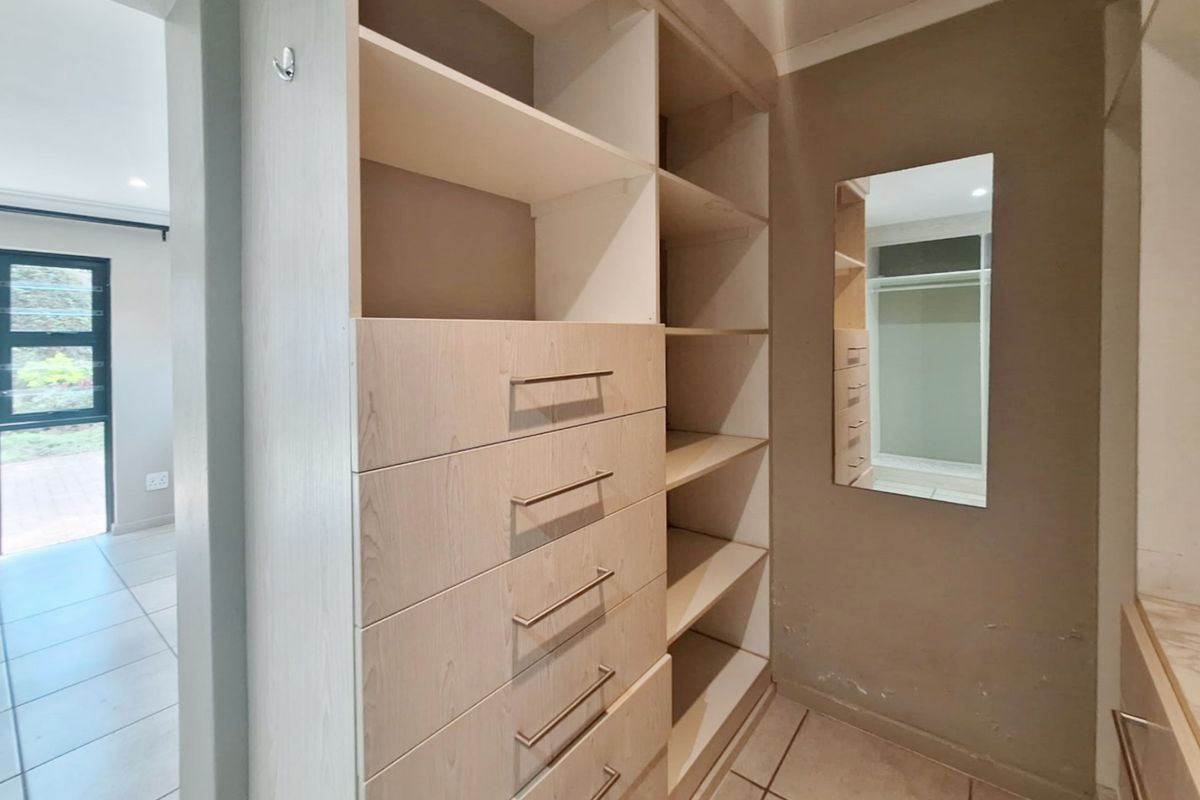 A walk-in closet area featuring built-in light wood cabinetry with drawers and shelving, finished with tiled flooring.