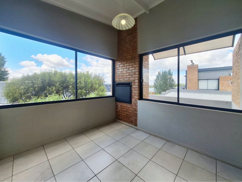 A bright, enclosed balcony or sunroom featuring tiled floors, an exposed brick wall with a built-in fireplace, and large windows offering natural light.