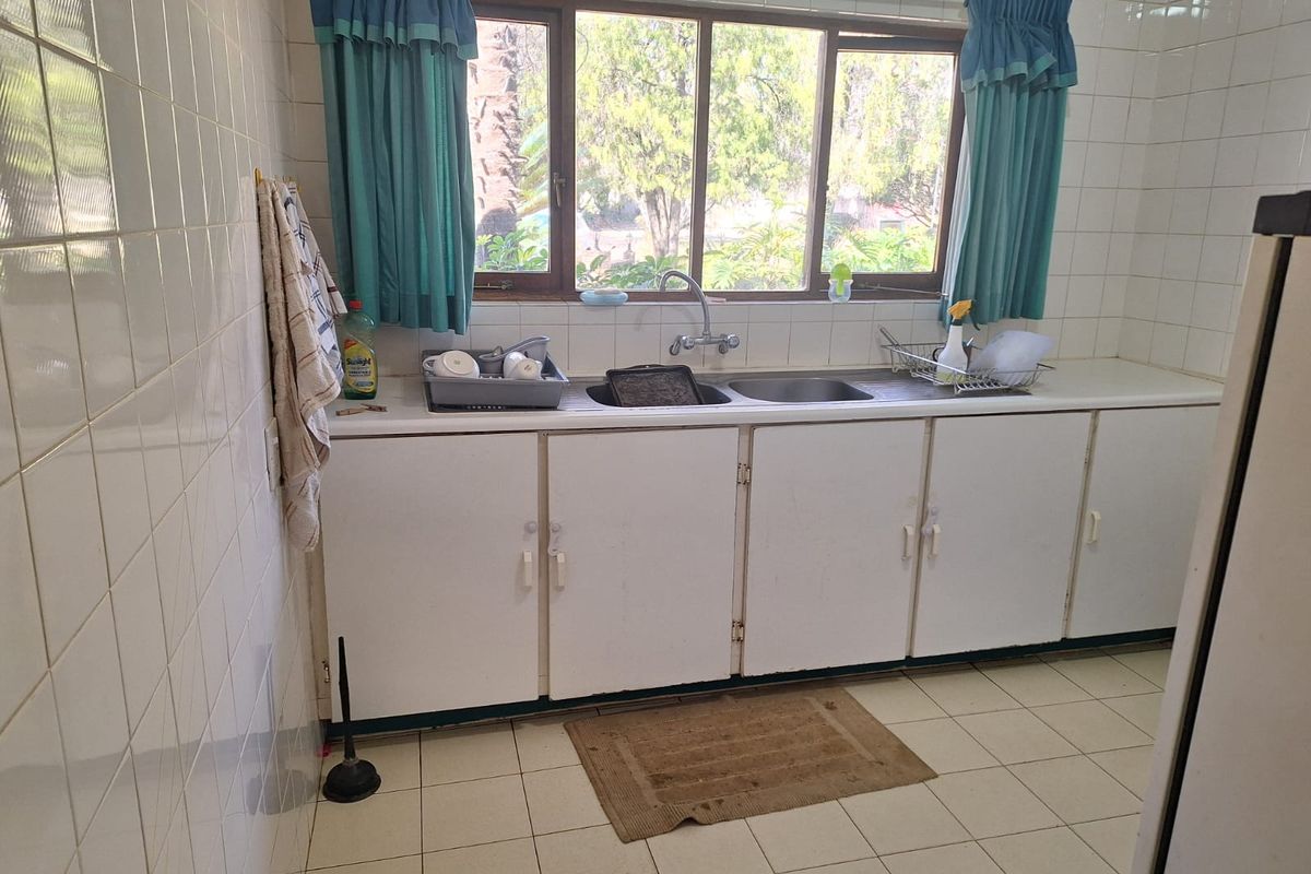 A functional kitchen area featuring a double basin sink, built-in white cabinetry, and tiled wall and floor finishes.