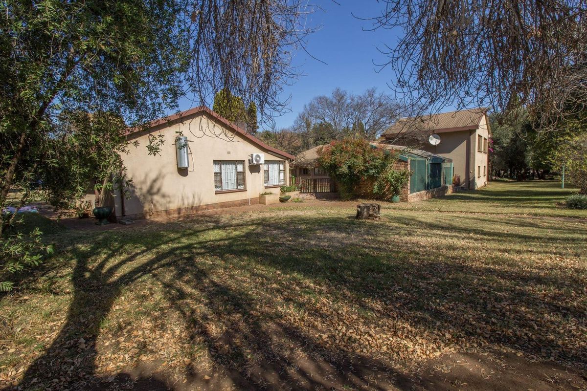 Rear view of the property showing the main dwelling and outbuildings set within a spacious garden with mature trees.
