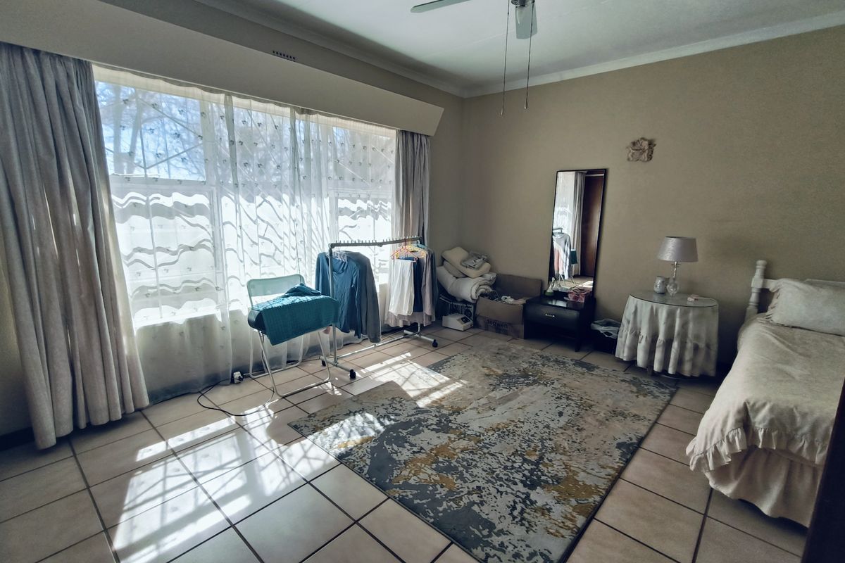 Spacious bedroom featuring large windows with natural light, tiled flooring, and a ceiling fan, offering a comfortable and functional living space.