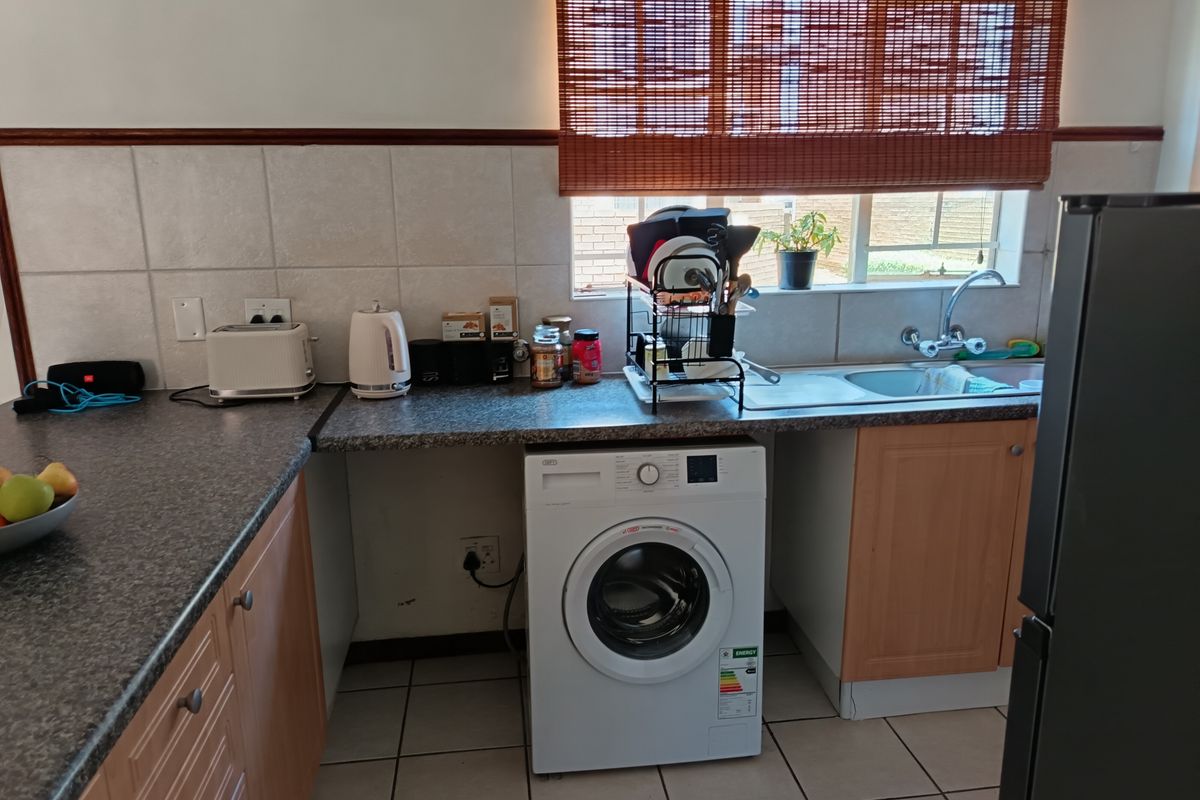 A functional kitchen area featuring laminate countertops, tiled backsplash, a stainless steel sink, and a dedicated space for a washing machine.