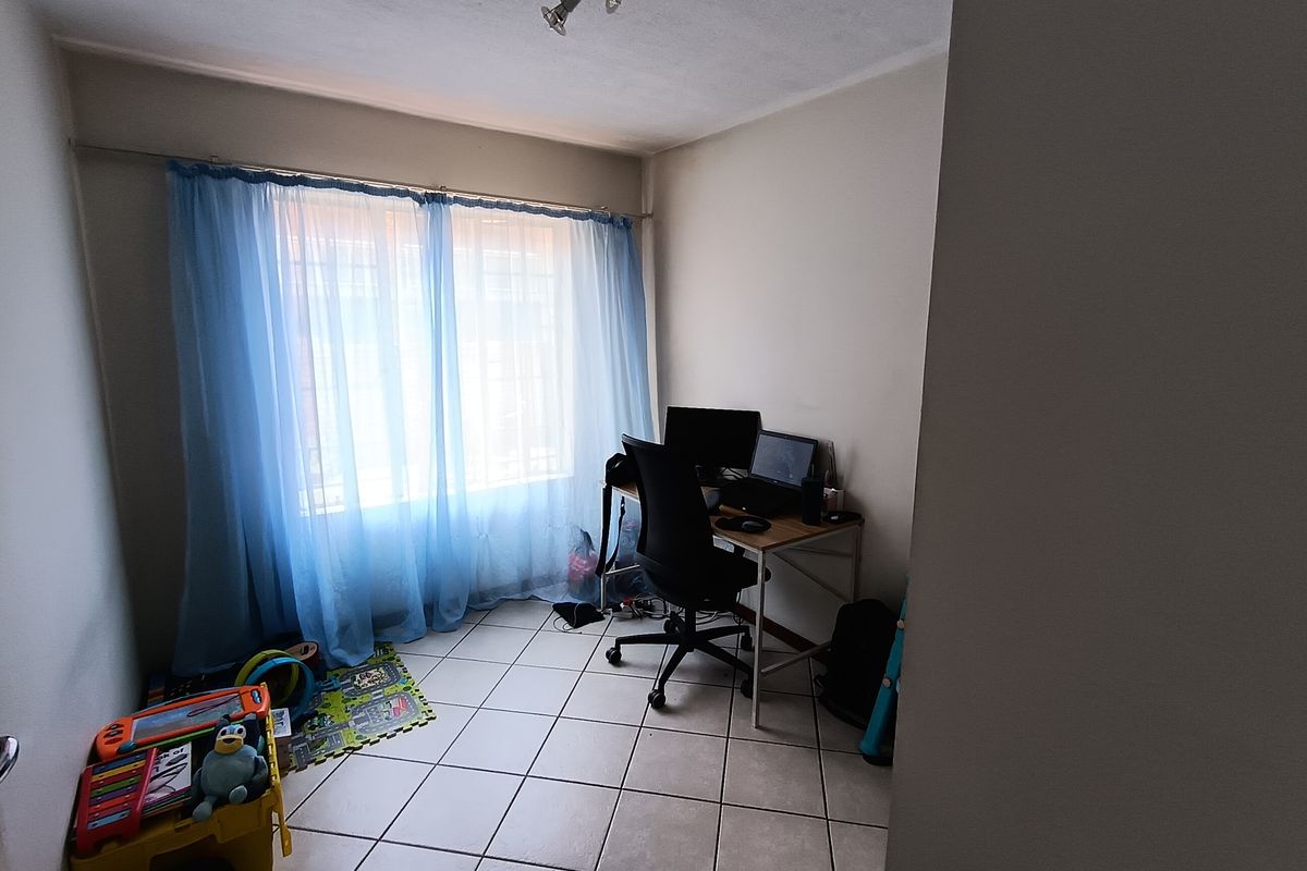 A functional bedroom or home office space featuring tiled flooring and a large window with security bars.
