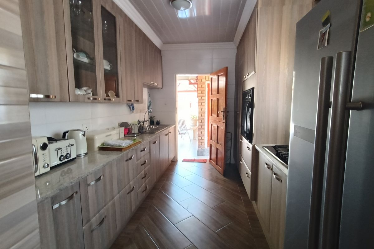 A galley-style kitchen featuring wood-grain cabinetry, stone-look countertops, built-in oven, and tiled flooring, with direct access to an outdoor area.